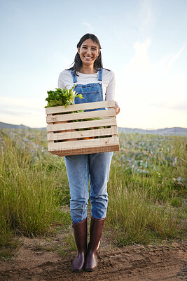 Buy stock photo Portrait of a woman farmer holding a wooden box of fresh vegetables. Young brunette female standing on a field while holding a basket of organic produce