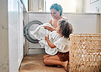 Young hispanic mother and her daughter sorting dirty laundry in the washing machine at home. Adorable little girl and her mother doing chores together at home