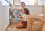 Young hispanic mother and her daughter sorting dirty laundry in the washing machine at home. Adorable little girl and her mother doing chores together at home