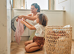 Young hispanic mother and her daughter sorting dirty laundry in the washing machine at home. Adorable little girl and her mother doing chores together at home