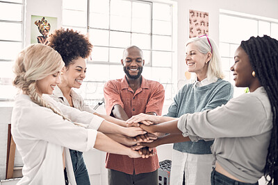 Group of five cheerful diverse businesspeople piling their hands together in an office at work. Happy business professionals having fun standing with their hands stacked for support and unity