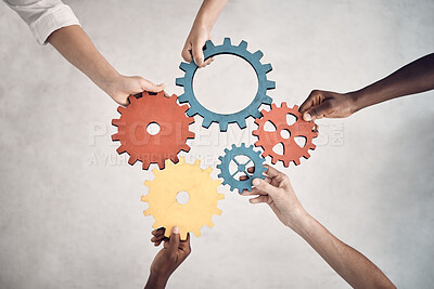 Group of five businesspeople holding and fitting gears together in an office at work. United business professionals having fun connecting gear pieces during a meeting