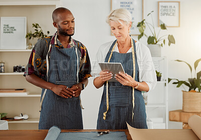 Buy stock photo Two designers using a digital tablet while working with material at work. Mature caucasian tailor talking and holding a digital tablet while working with a male african american colleague