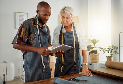 Buy stock photo Two designers using a digital tablet while working with material at work. Young african american tailor talking and holding a digital tablet while working with a female caucasian colleague