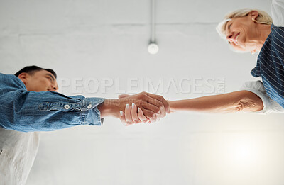 Buy stock photo Two clothing designers shaking hands while working together at a shop. Mature caucasian woman and young asian man giving each other a handshake at work. Colleagues greeting at work