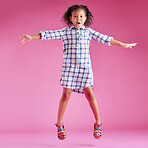 A pretty little mixed race girl with curly hair celebrating and dancing against a pink copyspace background in a studio. African child jumping and feeling free