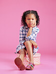 One cute little mixed race girl sitting in a studio and daydreaming against a pink copyspace background. A lonely African American child looking sad and depressed