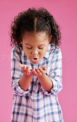 Buy stock photo A pretty little mixed race girl with curly hair blowing on coins  in her hands against a pink copyspace background in a studio. African child looking excited about her savings