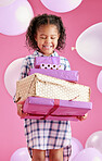A pretty little mixed race girl with curly hair holding a stack of wrapped presents against a pink copyspace background in a studio. African child looking excited about getting gifts for her birthday