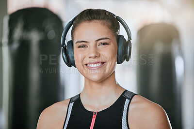 Portrait of smiling trainer alone in gym, listening to music on headphones. Beautiful happy caucasian coach standing during health club workout. Woman in routine training in exercise fitness centre