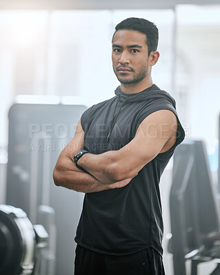 Portrait of one serious asian trainer alone in gym. Handsome focused coach standing with arms crossed after workout in health club. Young confident man in fitness centre for routine training exercise