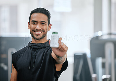 Portrait of smiling trainer alone in gym, holding and showing bottle of steroid pills. Asian coach with hormone enhancing drugs for workout in exercise health club. Bodybuilder man in fitness centre