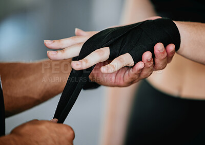 Closeup of unknown mixed race trainer wrapping caucasian boxer’s hands in gym. Hispanic coach getting kickboxer ready with hand wrap to fight in self defence in health club workout. Two fit people