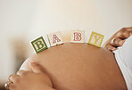 Close up of pregnant woman showing her belly while lying down with wooden play blocks with baby lettering on it