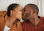 Close up of a loving african american couple kissing while lying together on a bed, from above. Happy young man and woman sharing romantic intimate moment at home