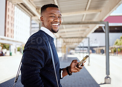 Portrait of Black businessman travelling alone. A young african american businessman waiting for a train at a railway station and using his wireless cellphone during his commute at a train station