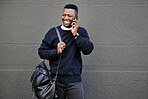 African american male on a phone call with his mobile device outside a building during the day while smiling Young black male talking on a phone while commuting to work