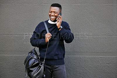 African american male on a phone call with his mobile device outside a building during the day while smiling Young black male talking on a phone while commuting to work