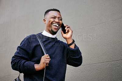 African american male on a phone call with his mobile device outside a building during the day while smiling Young black male talking on a phone while commuting to work