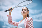 Close up of beautiful hispanic female tennis player holding tennis racket over her head while standing against a blue sky. Sportswoman looking serious and ready for a game of tennis