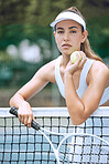 Dedicated young female tennis player holding a tennis racket and ball while leaning over a net. Hispanic woman ready for her tennis match at the club. Sportswoman ready for tennis practice