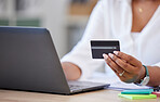 Closeup of a businesswoman holding and using a credit card and typing on a laptop alone at work. One hispanic female businessperson making an online purchase with her debit card and laptop