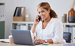 Mixed race businesswoman on a call using a phone while working on a laptop alone at work. One hispanic businesswoman talking on a cellphone while working on a computer at a desk in an office