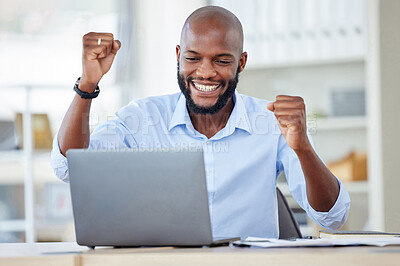 Young happy african american businessman cheering with joy and working on a laptop in an office at work alone. One cheerful male business professional cheering with his fists and using a computer while sitting at a desk