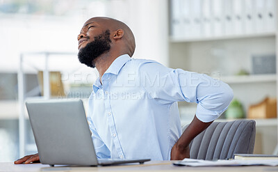 Unhappy african american businessman suffering from bad back pain in an office at work alone. One tired male business professional touching his sore back while sitting at a desk