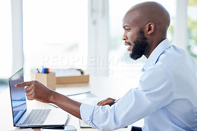 Young african american businessman pointing his finger and working on a laptop in an office alone at work. One male businessperson using a laptop at a table at work