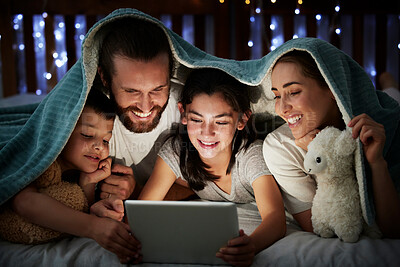 Buy stock photo Happy caucasian family with two children using digital tablet lying under blanket in the dark at night with their faces illuminated by device screen light. Family of four reading online story or watching video before bedtime