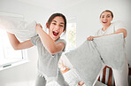 Portrait of cute teenage daughter and mother having a fun pillow fight at home. Happy young girl and mother holding pillows and standing on bed playing and enjoying free time together in the morning