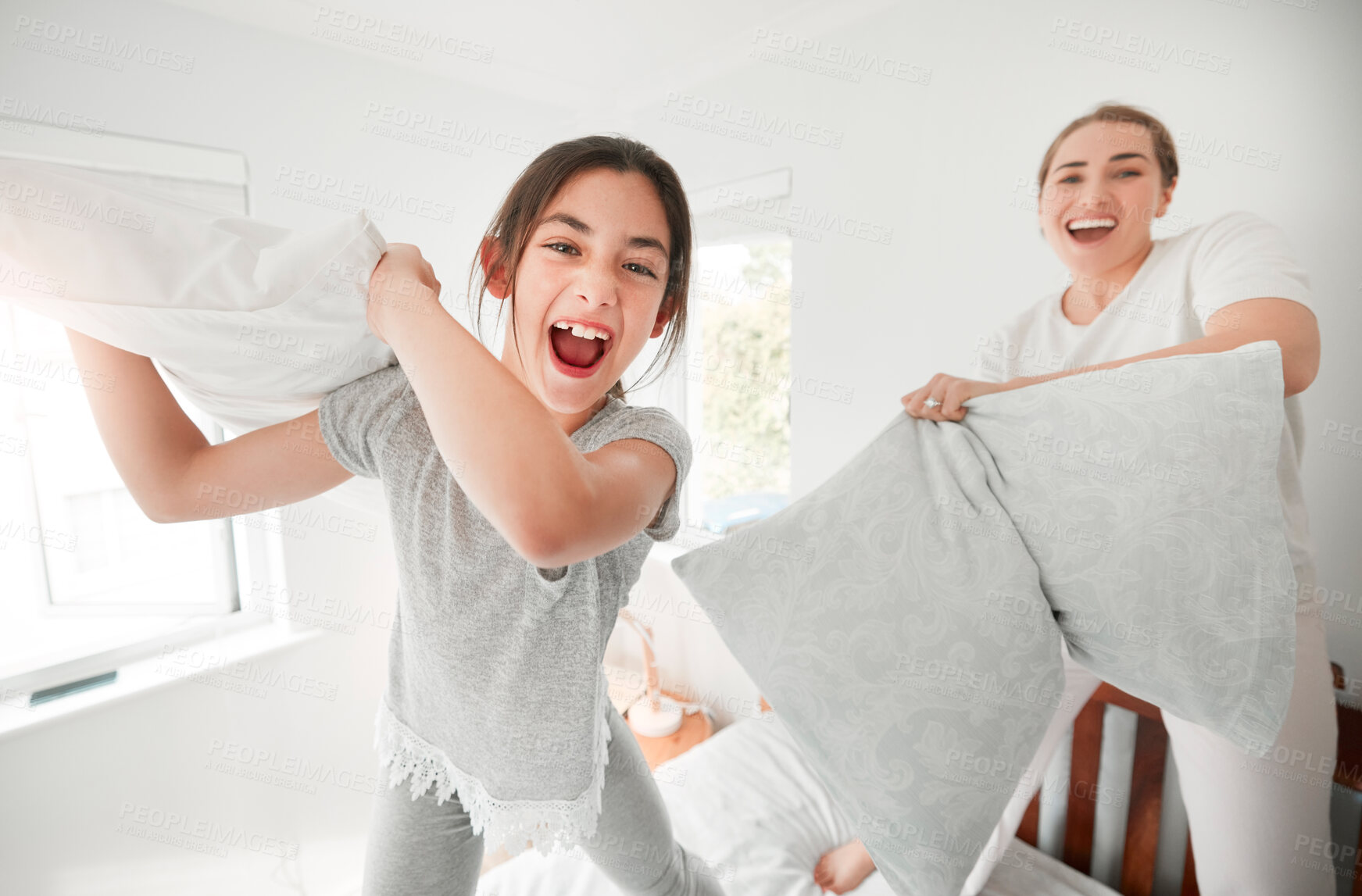 Buy stock photo Portrait of cute teenage daughter and mother having a fun pillow fight at home. Happy young girl and mother holding pillows and standing on bed playing and enjoying free time together in the morning