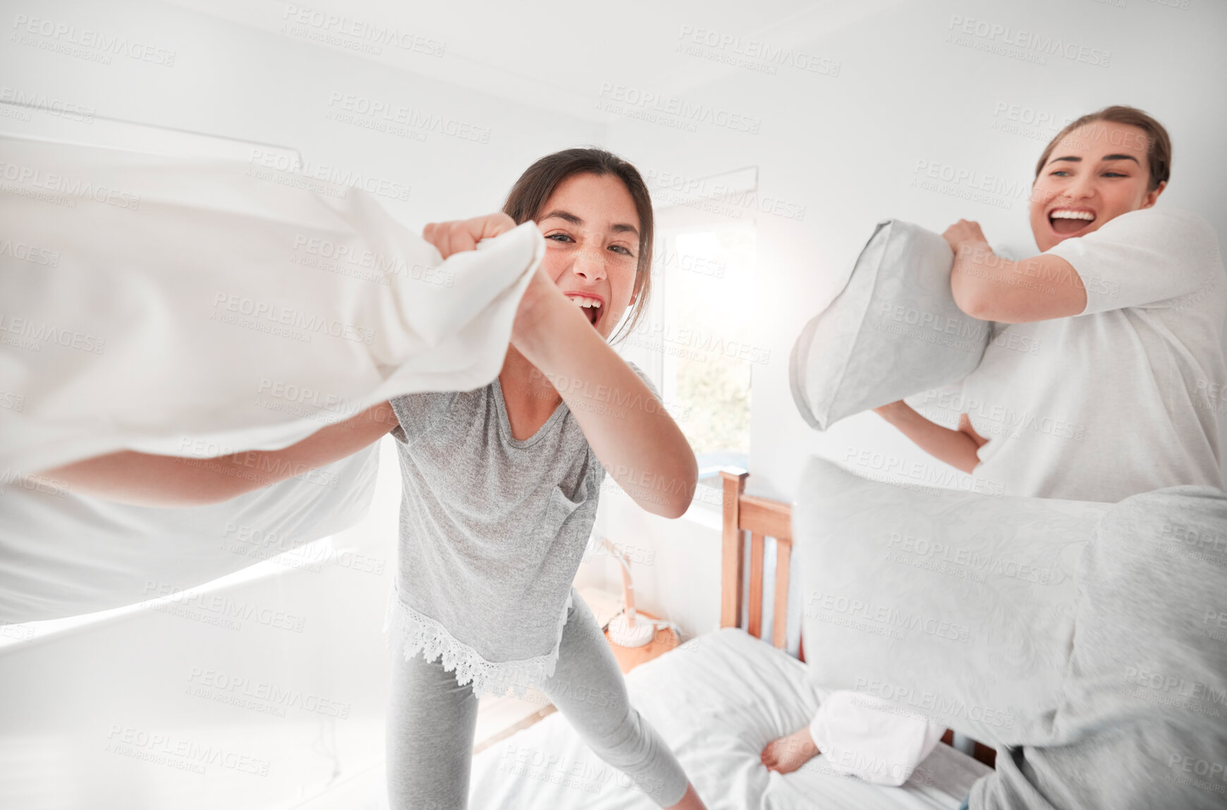 Buy stock photo Portrait of adorable teenage daughter and mother having a fun pillow fight at home. Happy young girl and mother holding pillows and standing on bed playing and enjoying free time together in the morning