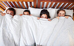 Above view of happy young caucasian family with two children lying in bed and pulling blanket over their noses. Two parents with daughter and son spending time and having a lazy morning peeking from under white comforter
