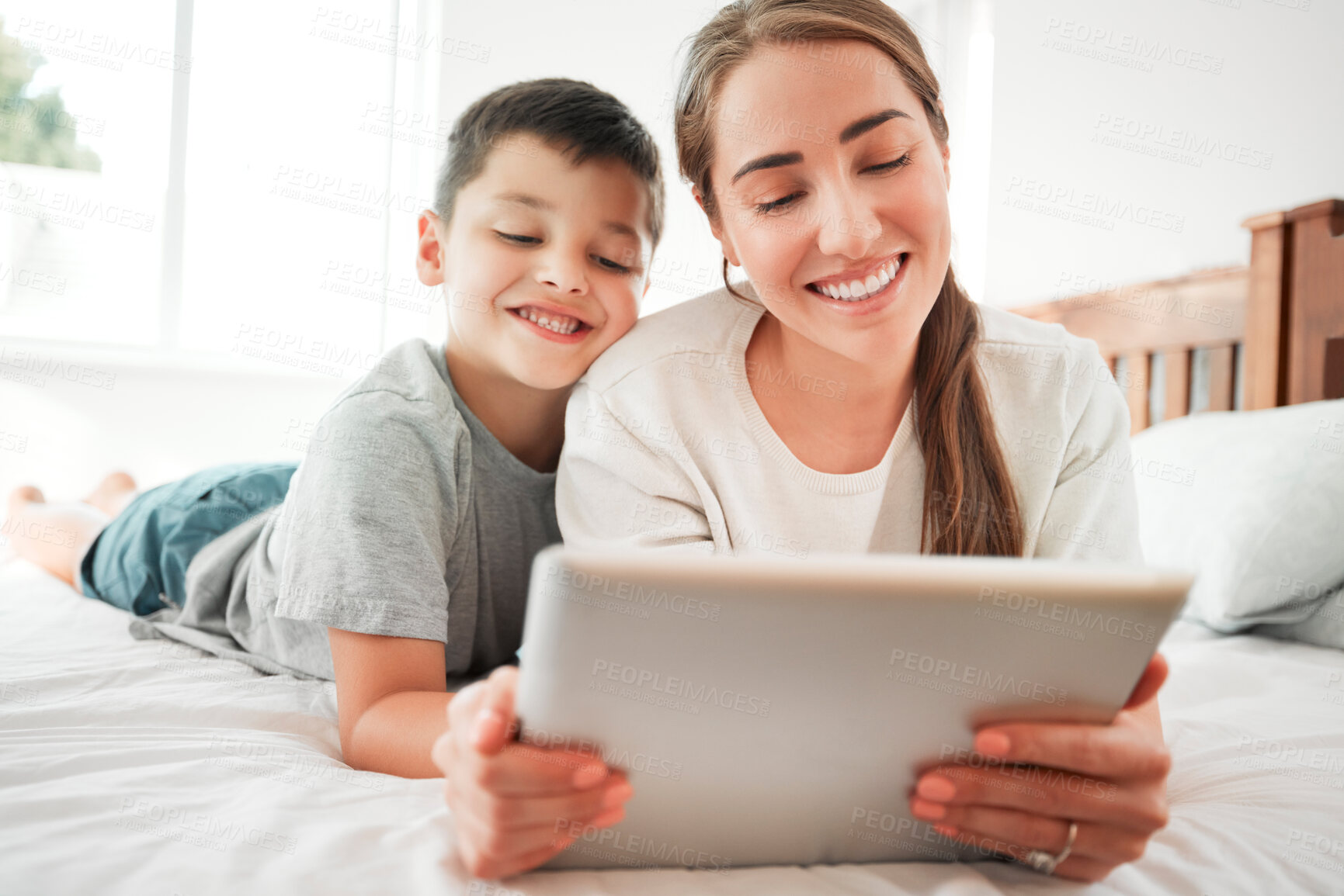 Buy stock photo Happy caucasian mother and son holding digital tablet while lying together on a bed. Little boy and mom watching movie online or playing game while spending time at home