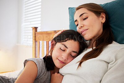 Loving caring mother sitting on a bed while her teenage daughter puts her head on her chest and falls asleep. Young caucasian mom bonding with her child at home embracing and showing love