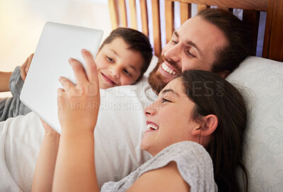 Happy caucasian father lying in bed with his two children using digital tablet and watching movie, reading online book or playing games together at home. Young dad spending time with his daughter and son on the weekend