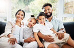 Portrait of a young hispanic family happily bonding together on the sofa at home. Mixed race mother and father sitting of the couch in the loung and looking happy while bonding with their cute little son and daughter