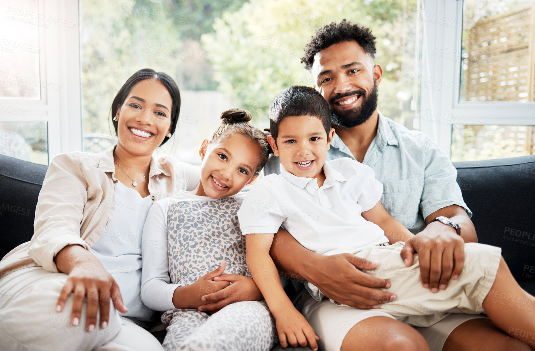 Buy stock photo Portrait of a young hispanic family happily bonding together on the sofa at home. Mixed race mother and father sitting of the couch in the loung and looking happy while bonding with their cute little son and daughter
