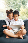 Closeup of a mixed race brother and sister playing together using their digital tablet on the sofa at home. Hispanic cute little boy and girl using a wireless device while sitting on the couch in the lounge