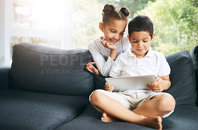 Buy stock photo Closeup of a mixed race brother and sister playing together using their digital tablet on the sofa at home. Hispanic cute little boy and girl using a wireless device while sitting on the couch in the lounge
