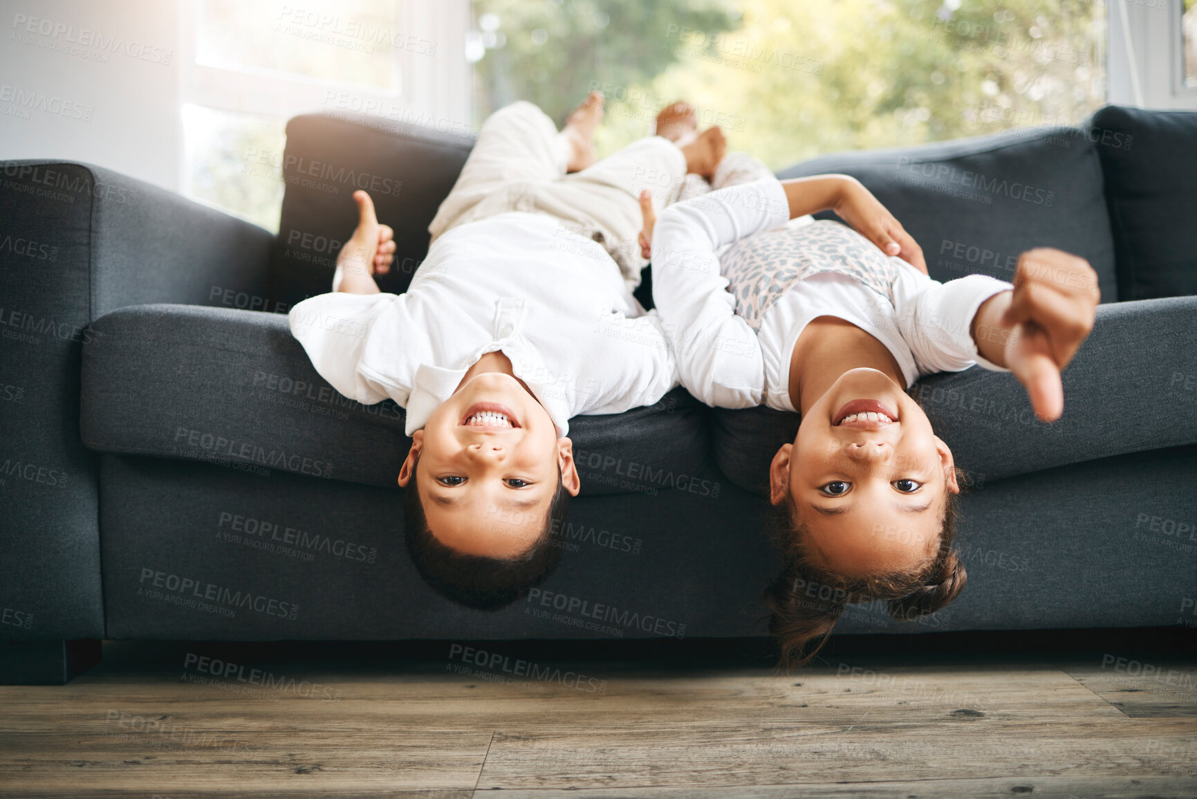 Buy stock photo Portrait of two little mixed race siblings spending time together lying upside down at home. Cute hispanic girl and boy playing on the couch in the lounge