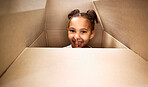 Portrait of a cute little hispanic girl playing with a cardboard box in a new apartment. Cute mixed race girl hiding in a box and smiling in a house. Relocation and moving day of big family