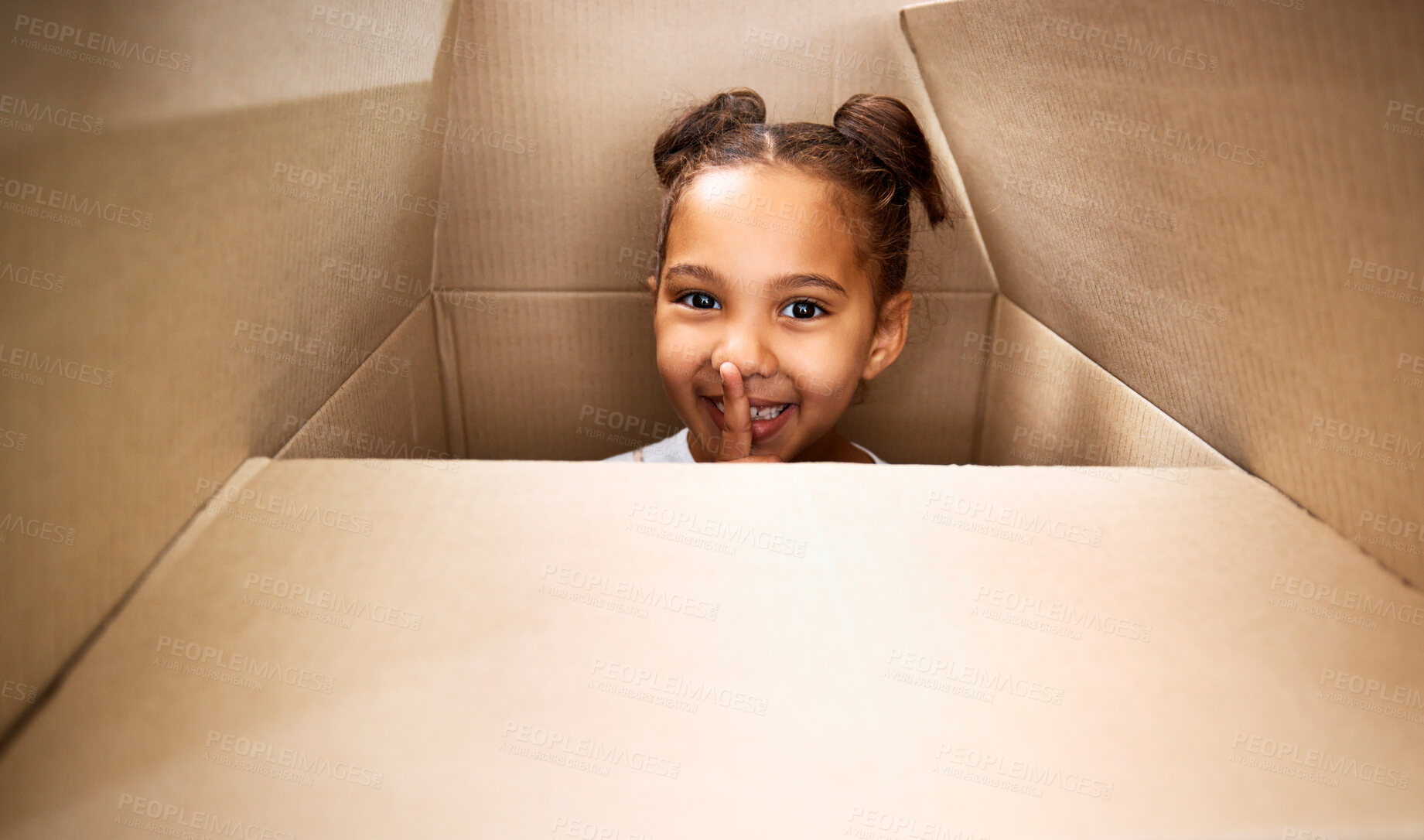 Buy stock photo Portrait of a cute little hispanic girl playing with a cardboard box in a new apartment. Cute mixed race girl hiding in a box and smiling in a house. Relocation and moving day of big family