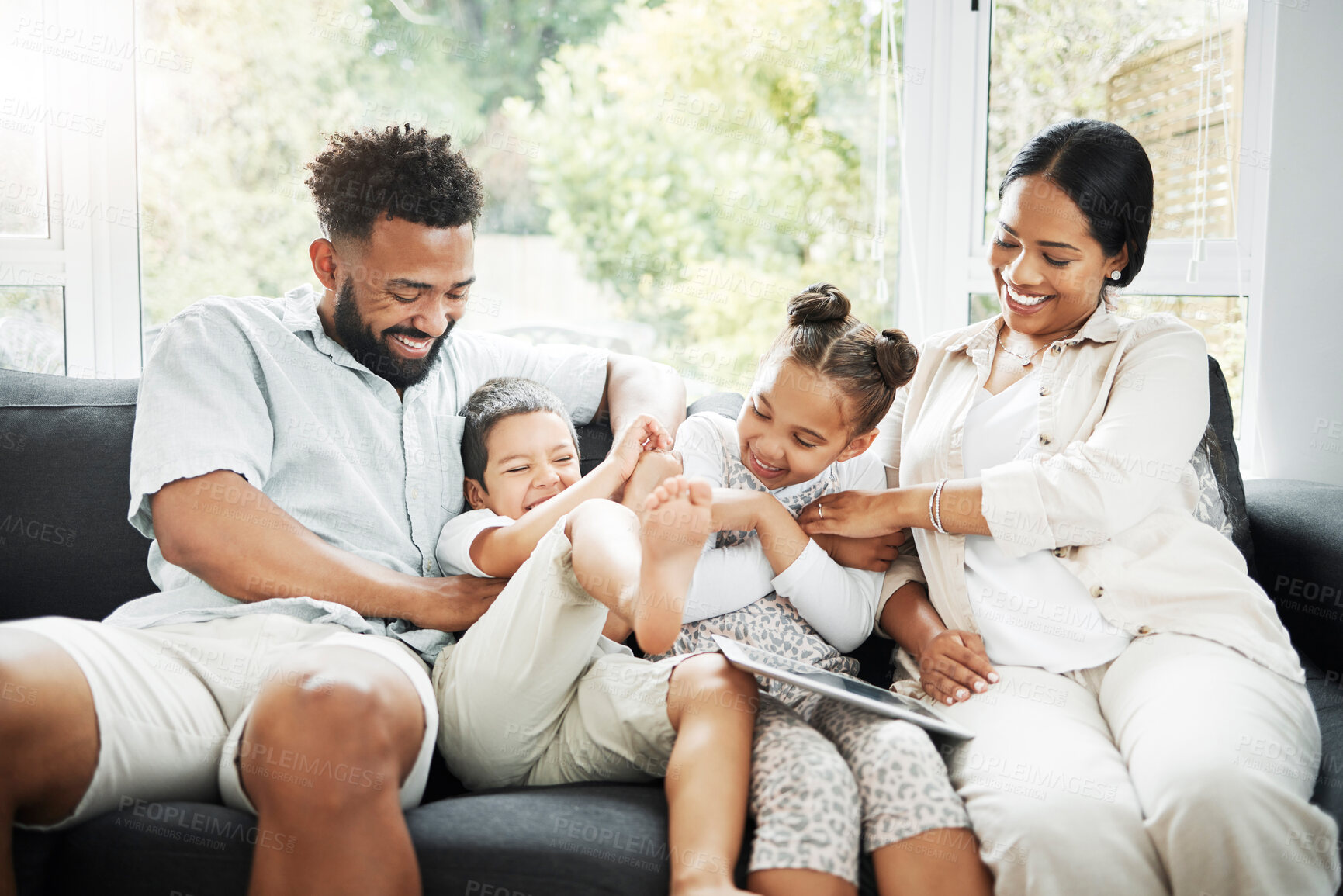 Buy stock photo A young hispanic family happily bonding together on the sofa at home. Mixed race mother and father sitting of the couch in the loung and looking happy while bonding with their cute little son and daughter