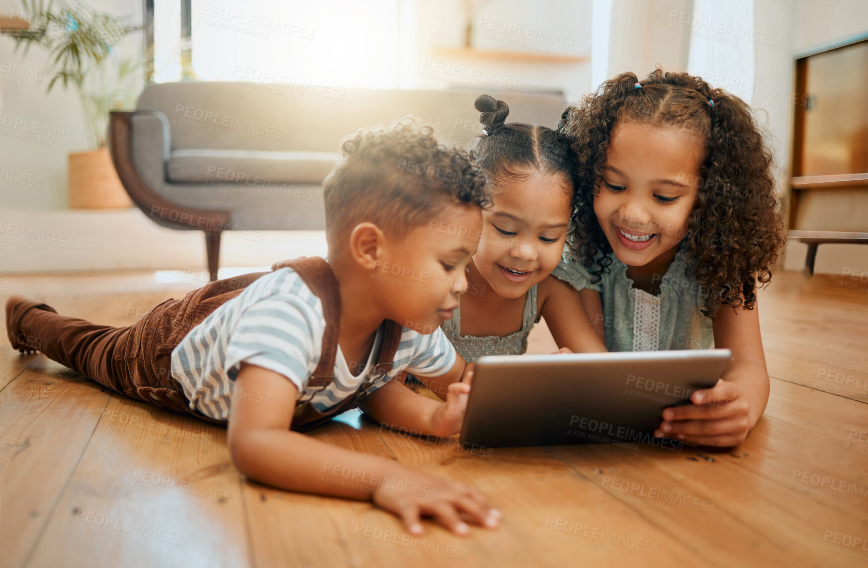 Buy stock photo Three happy mixed race siblings relaxing on the lounge floor together while using a digital tablet. Three kids playing games on a digital device at home