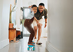 A happy mixed race family of two playing and skating on the  lounge floor together. Loving black single parent bonding with his son while teaching him  how to balance on a skateboard at home