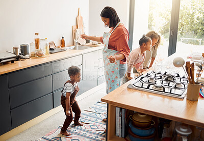 A happy mixed race family of five cooking and having fun in a kitchen together. Loving black single parent bonding with her kids while teaching them domestic skills at home