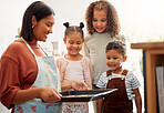 A happy mixed race family of five cooking and having fun in a  kitchen together. Loving black single parent bonding with her kids while teaching them domestic skills at home